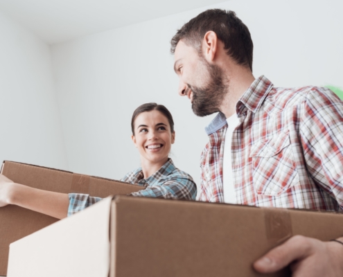 A couple smiling and carrying boxes into their apartment